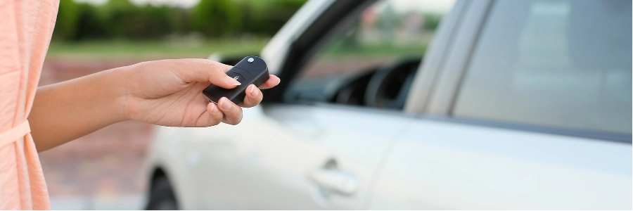 Person holding a car key fob in front of a car.